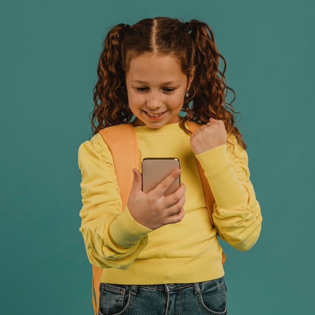 Niña de la escuela con camisa amarilla mirando su teléfono