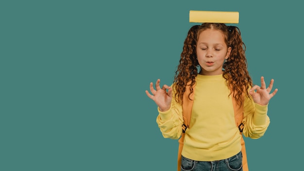 Niña de la escuela con camisa amarilla sosteniendo un libro en el espacio de copia de cabeza