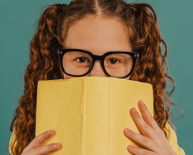 Niña de la escuela con camisa amarilla sosteniendo un libro
