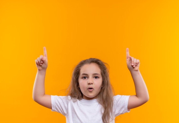 niña de la escuela con camiseta blanca puso su dedo en la pared naranja aislada