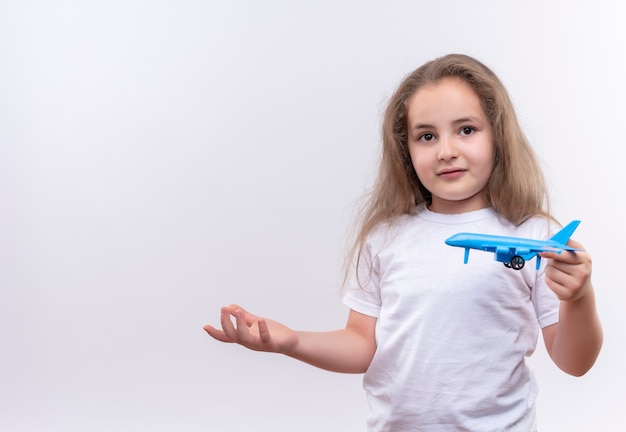 Niña de la escuela con camiseta blanca sosteniendo un plan de juguete en una pared blanca aislada