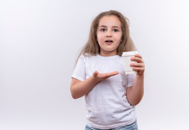 Niña de la escuela con camiseta blanca sosteniendo una taza de café en la pared blanca de aislamiento