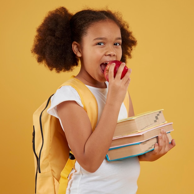 Niña de la escuela comiendo una manzana y sosteniendo libros