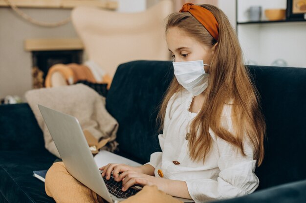 Niña de la escuela estudiando en casa con máscara, aprendizaje a distancia