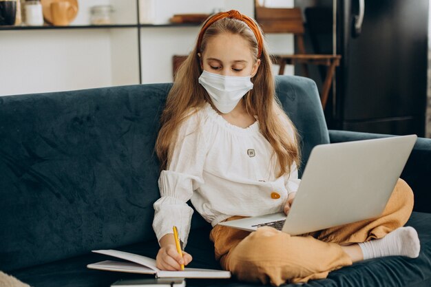 Niña de la escuela estudiando en casa con máscara, aprendizaje a distancia