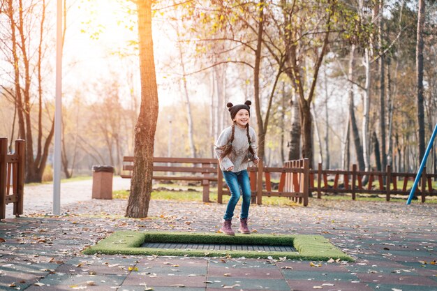 Niña de la escuela feliz saltando en un pequeño trampolín en el parque