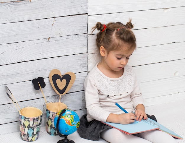 niña de la escuela se sienta en una madera blanca con un globo en sus manos y un cuaderno