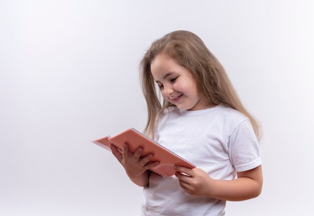 Niña de la escuela sonriente vistiendo camiseta blanca mirando portátil sobre fondo blanco aislado