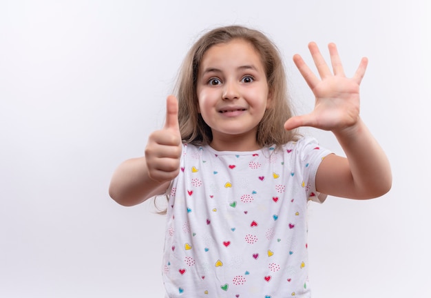 Niña de la escuela sonriente vistiendo camiseta blanca mostrando diferentes gestos sobre fondo blanco aislado