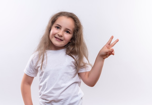 Niña de la escuela sonriente vistiendo camiseta blanca mostrando gesto de paz sobre fondo blanco aislado