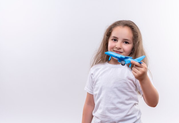 Niña de la escuela sonriente vistiendo camiseta blanca con plan de juguete sobre fondo blanco aislado