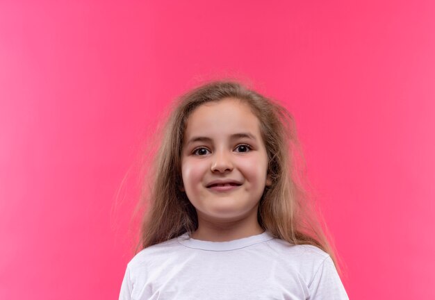 Niña de la escuela sonriente vistiendo camiseta blanca sobre fondo rosa aislado