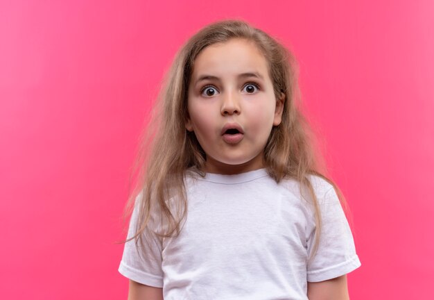 Niña de la escuela sorprendida con camiseta blanca sobre fondo rosa aislado