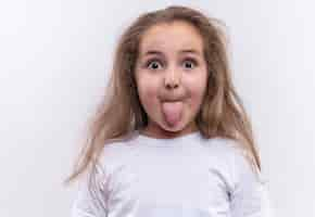 Foto gratuita niña de la escuela sorprendida vistiendo camiseta blanca mostrando lengua sobre fondo blanco aislado