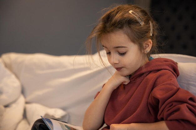 Una niña está leyendo un libro mientras está sentada en su habitación.