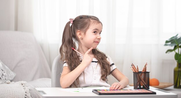 La niña está sentada a la mesa y haciendo los deberes. El niño aprende en casa. Educación en casa. Espacio para texto.