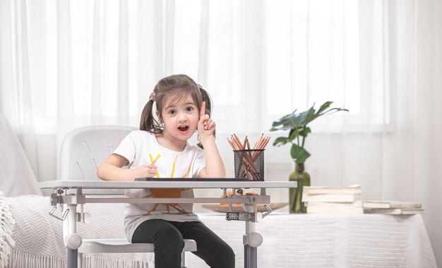 La niña está sentada a la mesa y haciendo los deberes. El niño aprende en casa. Educación en casa. Espacio para texto.