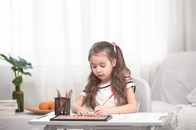 La niña está sentada a la mesa y haciendo los deberes.