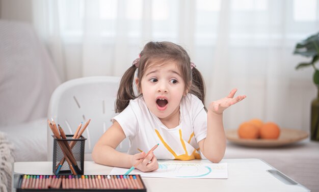 La niña está sentada a la mesa y haciendo los deberes.