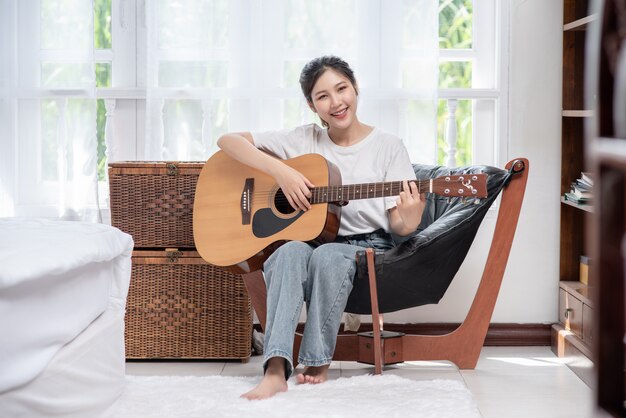 La niña está sentada y tocando la guitarra en la silla.