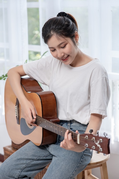 La niña está sentada y tocando la guitarra en la silla.