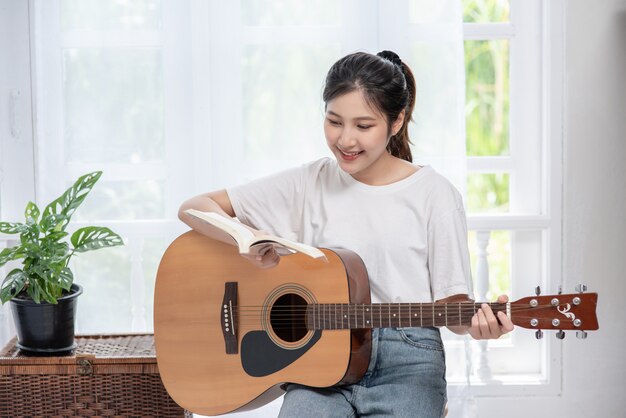 La niña está sentada y tocando la guitarra en la silla.