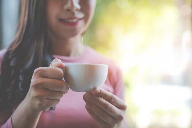 La niña está tomando café con placer en la cafetería.