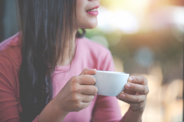 La niña está tomando café con placer en la cafetería.