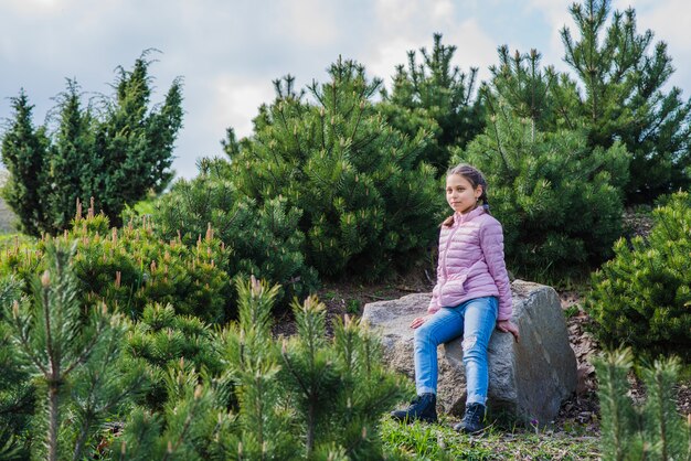 Niña estilosa sentada rodeada de vegetación