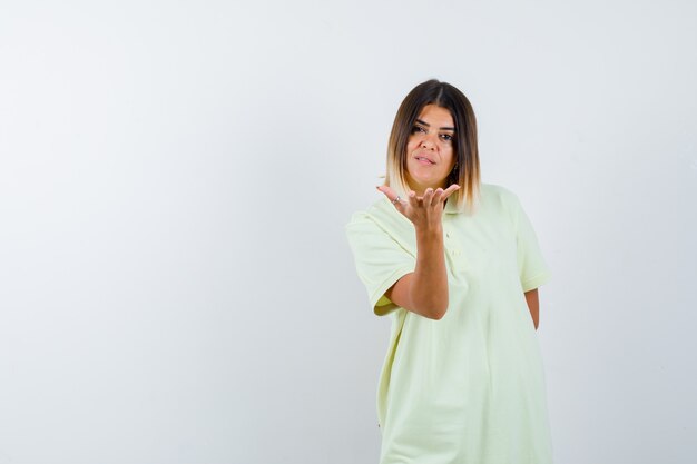 Niña estirando la mano hacia la cámara mientras sostiene algo en una camiseta y parece serio. vista frontal.