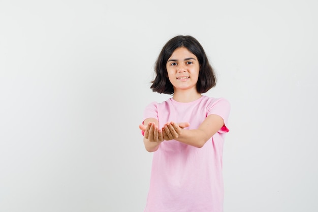 Niña estirando las manos ahuecadas en camiseta rosa y mirando alegre. vista frontal.