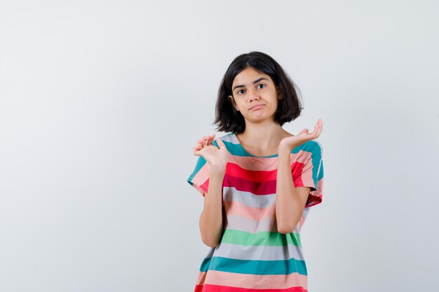 Niña estirando las manos en forma de cuestionamiento en camiseta, jeans y mirando confundido. vista frontal.