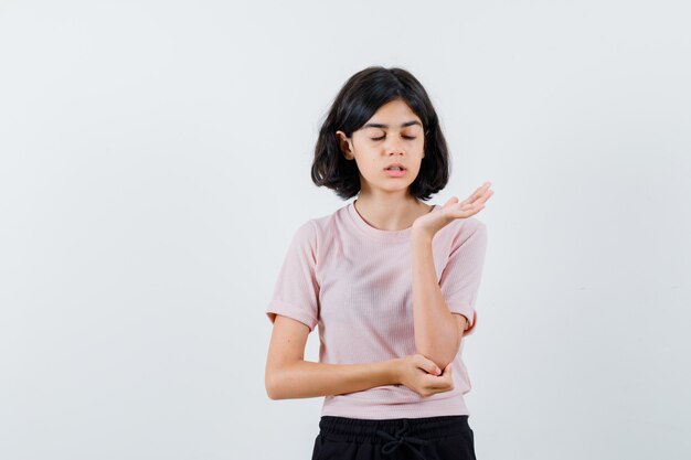 Niña estirando las manos mientras sostiene algo imaginario mientras cierra los ojos en camiseta rosa y pantalón negro y se ve feliz