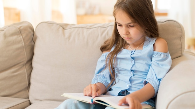 Niña estudiando en casa en el sofá con espacio de copia