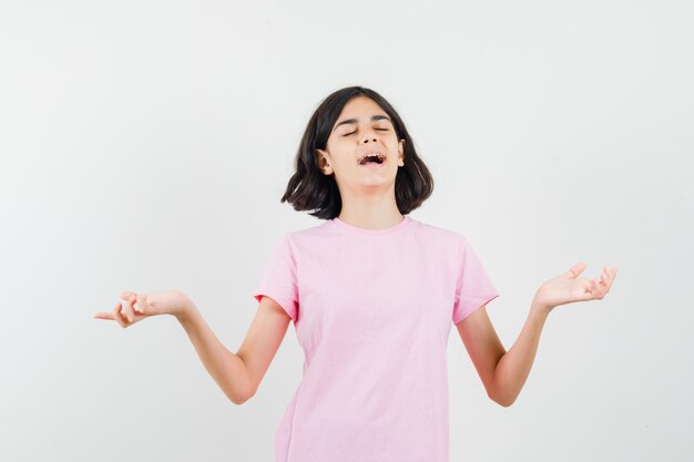 Niña extendiendo las palmas a un lado en camiseta rosa y luciendo pacífica. vista frontal.