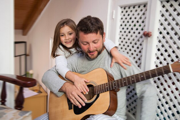 Niña feliz abrazando a su padre mientras sujeta una guitarra