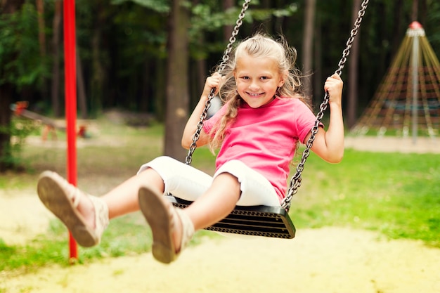 Niña feliz balanceándose en el patio de recreo