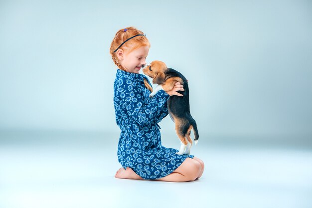 La niña feliz y un cachorro beagle en pared gris