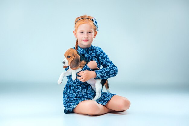 La niña feliz y un cachorro beagle en pared gris