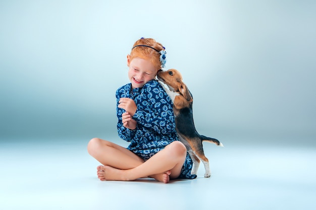 La niña feliz y un cachorro beagle en pared gris