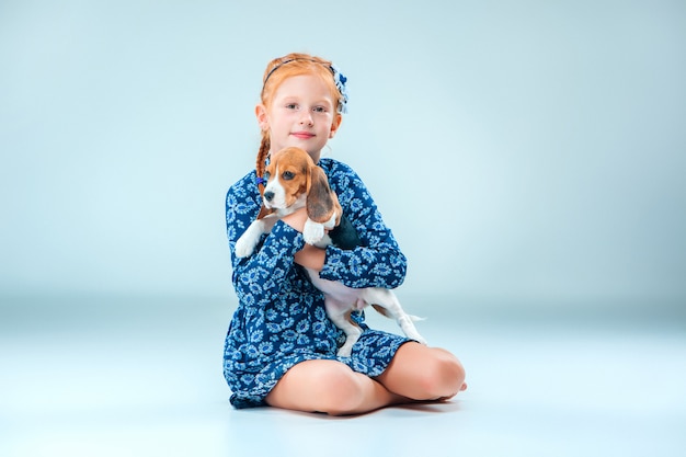 La niña feliz y un cachorro beagle en pared gris