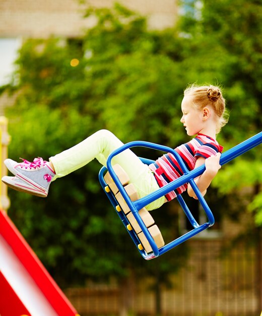 Niña feliz columpiandose en el parque infantil