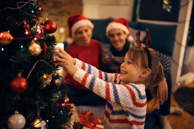 Niña feliz decorando el árbol de Navidad por la noche en casa