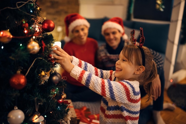 Niña feliz decorando el árbol de Navidad por la noche en casa