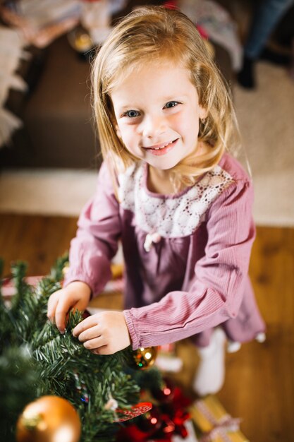 Niña feliz decorando árbol de navidad