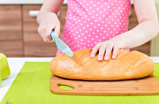 Niña feliz en delantal rosa cortando pan en la cocina.
