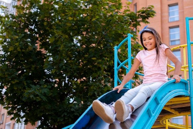 Niña feliz deslizándose sobre un tobogán en un patio de recreo