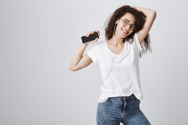 Niña feliz despreocupada bailando con música en auriculares, mediante teléfono móvil