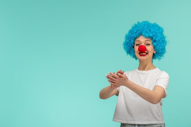 Niña feliz del día de los inocentes aplaudiendo sonriendo con la nariz roja en un disfraz de payaso cabello azul