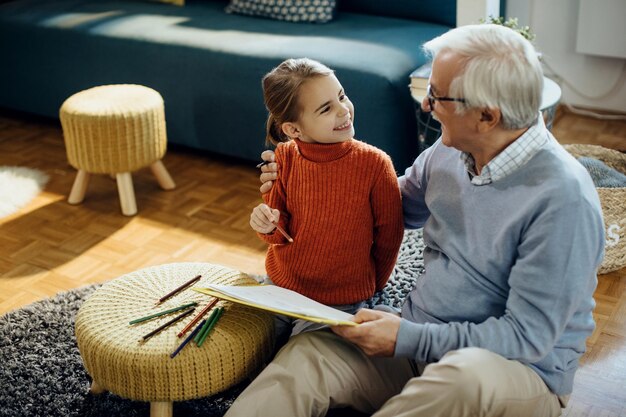 Niña feliz divirtiéndose mientras colorea con su abuelo en casa